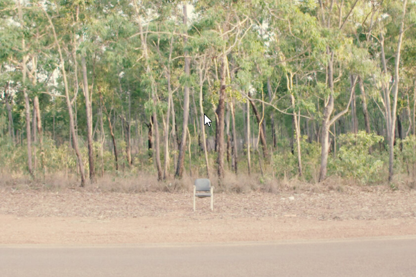 an office chair in front of a wood on a dusty road