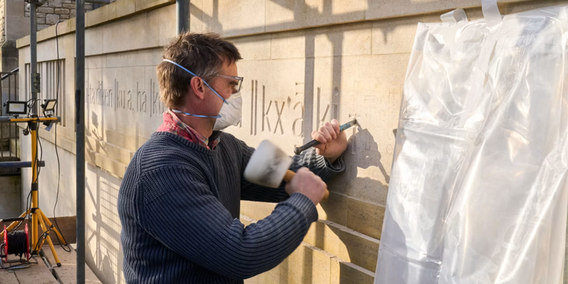 A stone mason carves the ǀxam words on a new building at Rhodes House