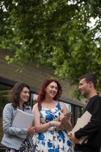 Three students outside smiling and chatting